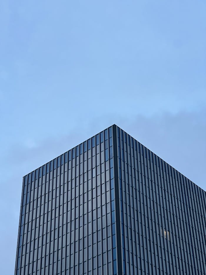 Low-angle view of a modern skyscraper with glass facade under a clear blue sky.