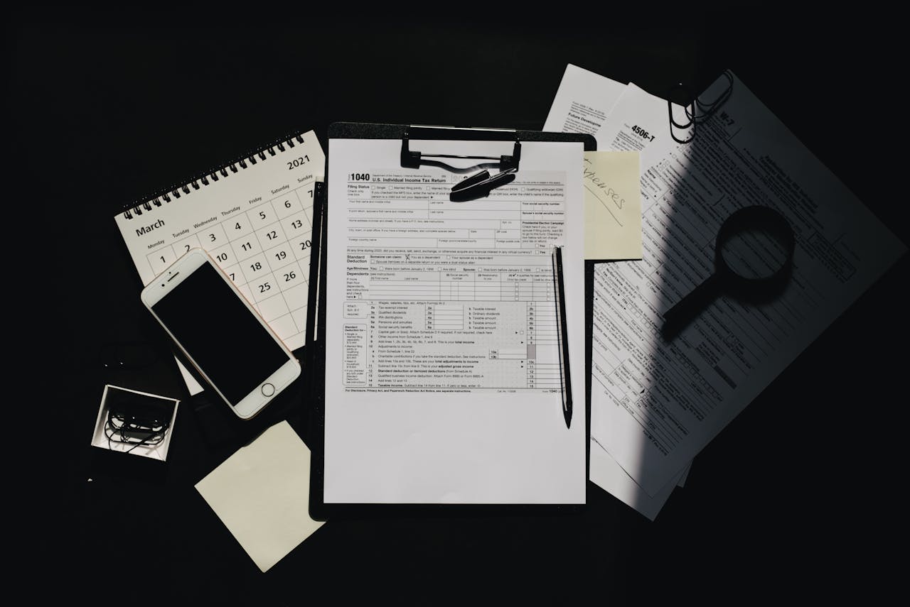 Flat lay of tax documents, calendar, and smartphone on a dark surface, symbolizing tax preparation.